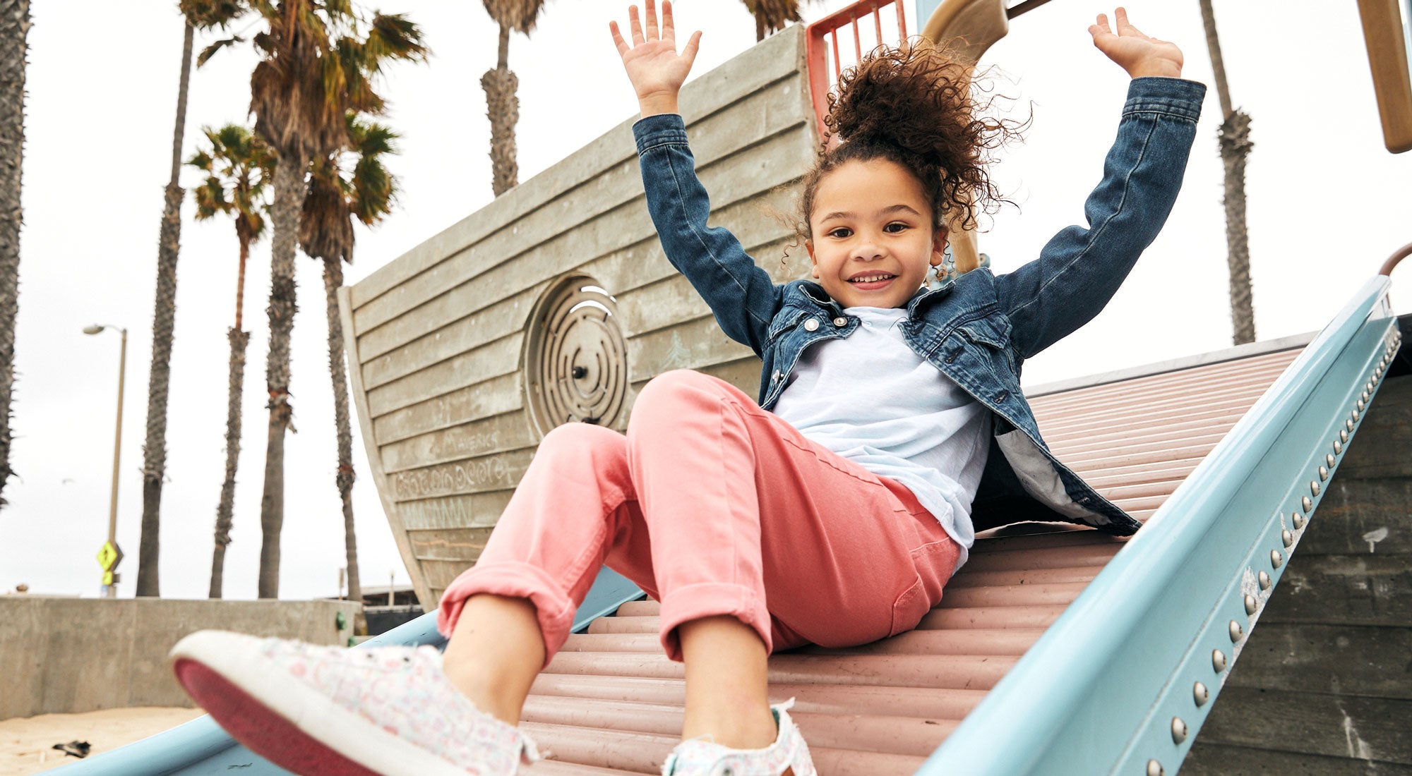 Girl sliding down at the playground with her hands up and having fun