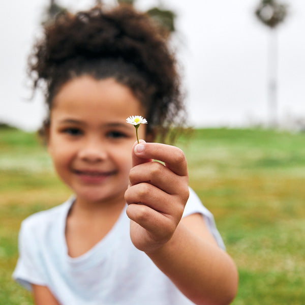 Girl in the Park Smiling and Holding Up a Flower