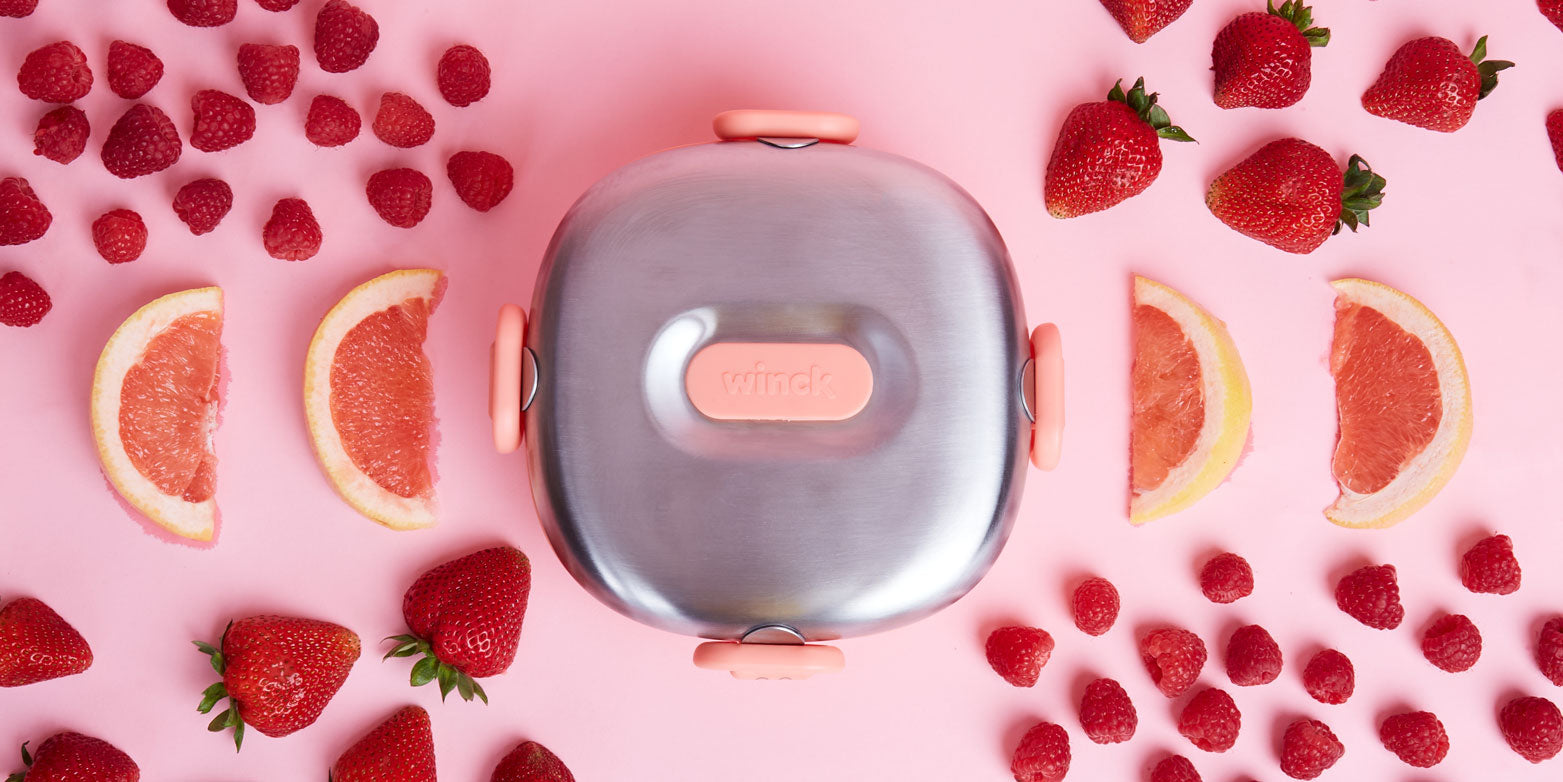 Winck Stainless Steel Bento Lunch Box for Kids with Fruits. The fruits are raspberries, strawberries and grapefruit that are arranged in a pattern beside the bento box. 