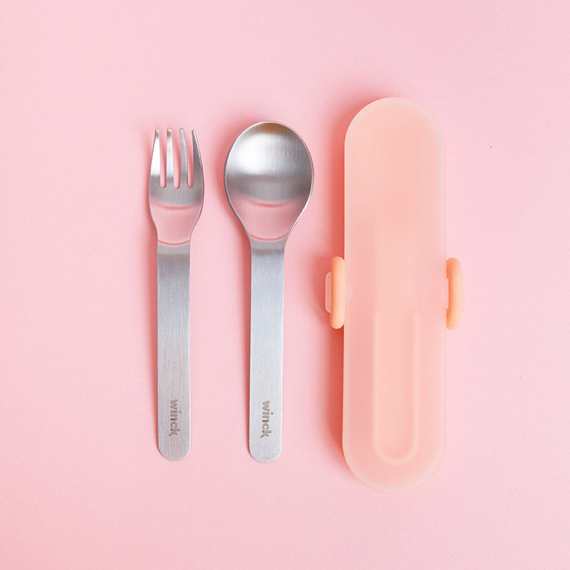 Winck Utensil Set for Kids in Peach. This includes Stainless Steel Fork and Spoon, and Carrying Case. It is on a soft pink background, showcasing a simple yet chic dining accessory for kids.