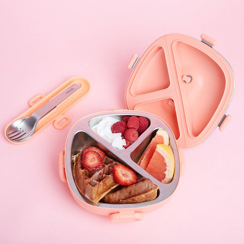 Open Winck Bento Box in Peach, filled with wholesome foods including waffles, fresh strawberries, raspberries, grapefruit, and a dollop of yogurt, accompanied by a matching fork and spoon set on a pink surface.